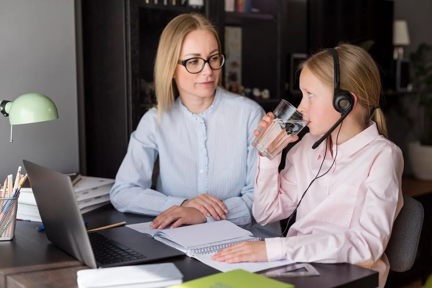 Маленькая девочка пьёт воду рядом с учителем.